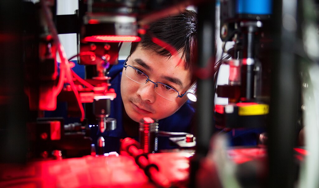 Close view shot of a man in glasses looking into a machine that has a glowing red light.