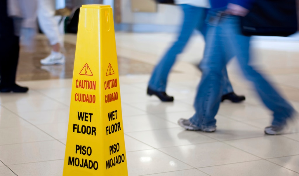 A yellow wet floor sign is posted on tile floor, in an interior location that shows the legs of people walking.